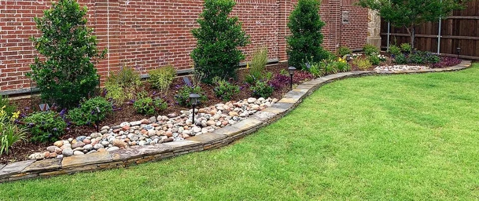 A landscape bed in McKinney, TX, with plants, mulch, and rock.